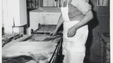 Mr L Feather in his bakery at Haworth making oatcake: turning the oatcake with a bent knife, after which it is transferred to the cooler end of the bakestone, shown on the left. Associated with the series of photographs used to illustrate "Life and Tradit