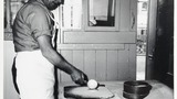 Mr L Feather in his bakery at Haworth making oatcake: pouring a ladleful of batter onto the scored bakboard. Associated with the series of photographs used to illustrate "Life and Tradition in West Yorkshire" (1976), cp.plates 98-102.